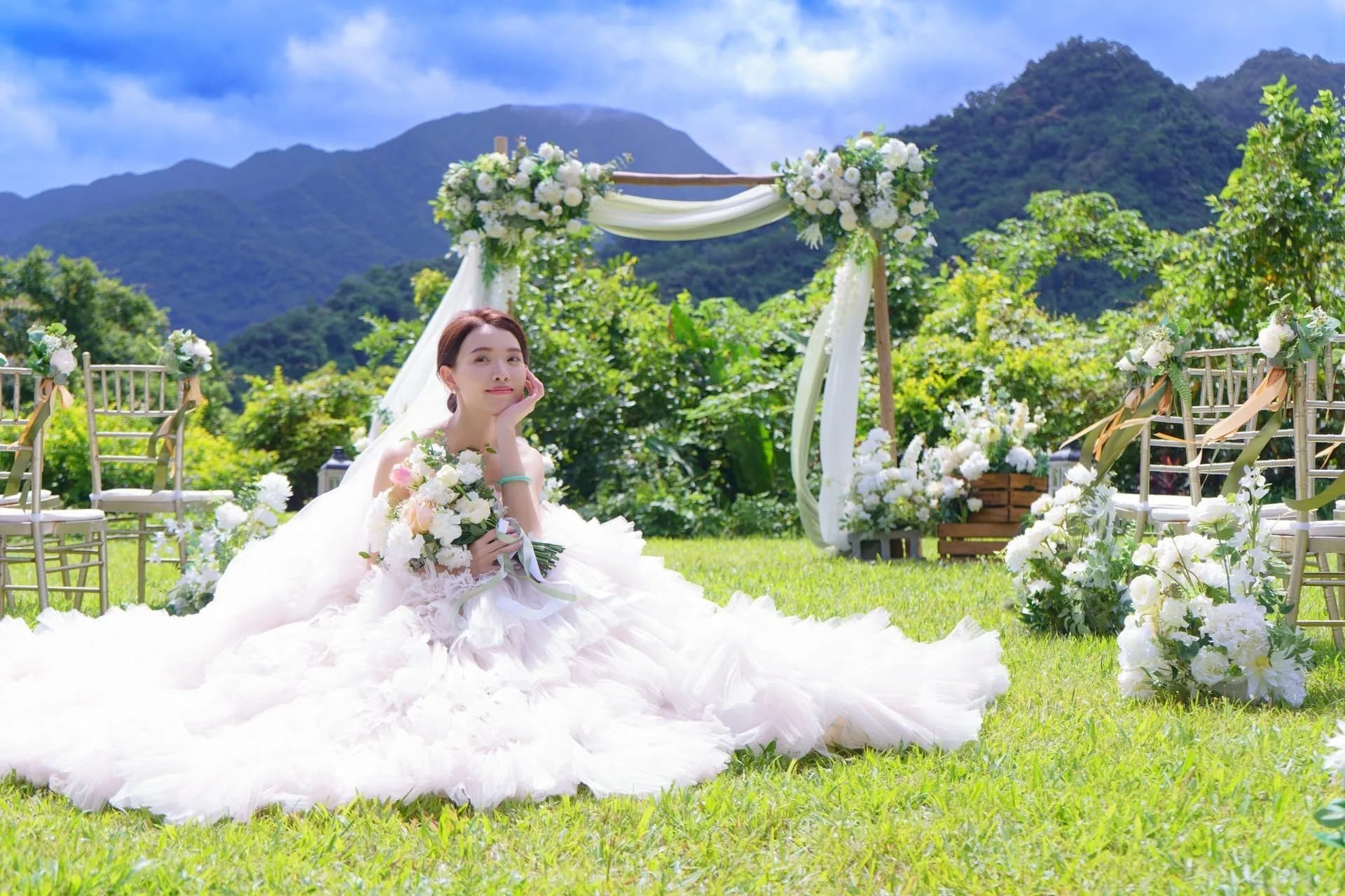 新娘坐於綠草地，手捧花束，白色婚紗與花藝拱門營造清新婚禮氛圍。